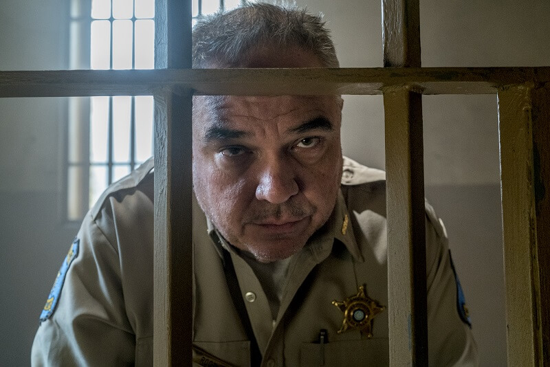 Sheriff Root sitting on outside of jail cell talking to unseen Cassidy in Preacher