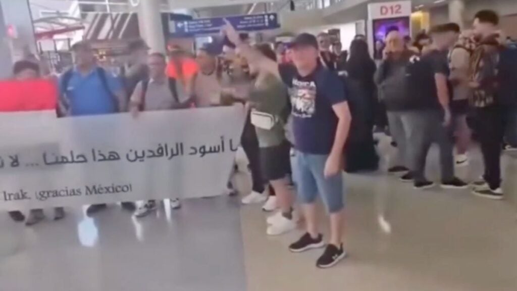 A group of fans holding a handmade bilingual banner at an airport gate are confronted by a man who grabs and tears it apart near Gate D12 at Dallas-Fort Worth International Airport.