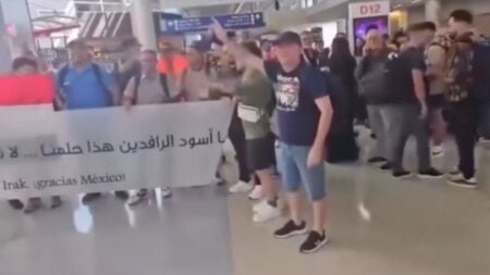 A group of fans holding a handmade bilingual banner at an airport gate are confronted by a man who grabs and tears it apart near Gate D12 at Dallas-Fort Worth International Airport.