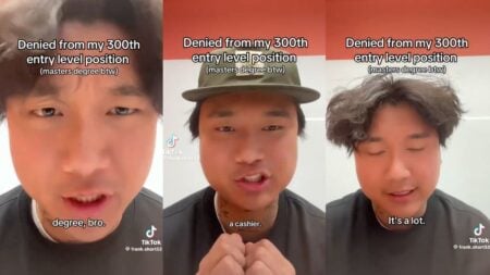 A tattooed man sits or stands in a casual setting filming himself on his phone, visibly frustrated as he discusses being rejected from hundreds of jobs including entry-level retail positions, despite holding a master's degree and accumulating over $120,000 in student debt.