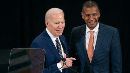 Former President Joe Biden and Jeffrey Scruggs at a podium during a portrait unveiling ceremony at Syracuse University in New York.