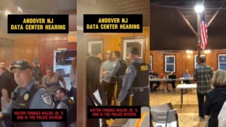 A man in a plaid shirt stands and addresses Andover Township Committee officials inside the Hillside Barn in Newton, New Jersey, gesturing emphatically as a packed crowd of residents looks on during a heated May 7, 2026 public meeting over a proposed AI data center, moments before a community member is arrested.