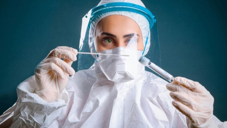Nebraska Panics as Quarantine Unit Receives 18 Americans From Hantavirus Ship: ‘Should I Start Stocking Up On Toilet Paper Now Or Later?’ A healthcare worker in protective gear holding a syringe, illustrating focus on safety and medical care.