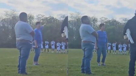 A still from a viral video taken at MacKay-Jaycees Park in Grand Rapids, Michigan, showing a woman yelling during a youth soccer game while players stand in a moment of silence on the field behind her.