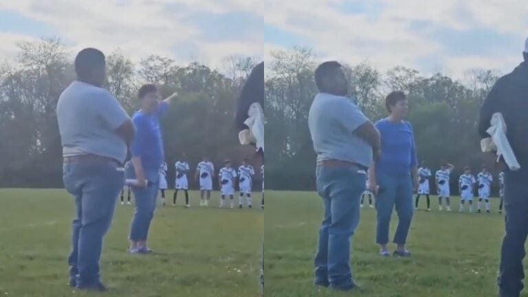 A still from a viral video taken at MacKay-Jaycees Park in Grand Rapids, Michigan, showing a woman yelling during a youth soccer game while players stand in a moment of silence on the field behind her.
