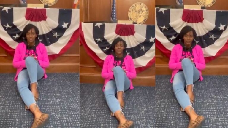 Florida State Representative Angie Nixon sits cross-legged on the floor of Governor Ron DeSantis' Capitol office lobby in Tallahassee, wearing her signature pink jacket, during a five-hour sit-in protest against newly passed congressional redistricting maps on May 15, 2026.