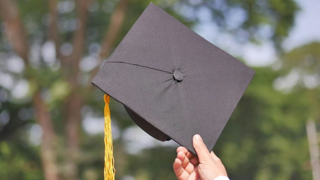 Texas School Under Fire After 6-Year-Old With Developmental Delay Is Allegedly Made to Watch Graduation Through Locked Doors: ‘This Is Heartbreaking’ A hand holding a graduation cap, symbolizing achievement and celebration.