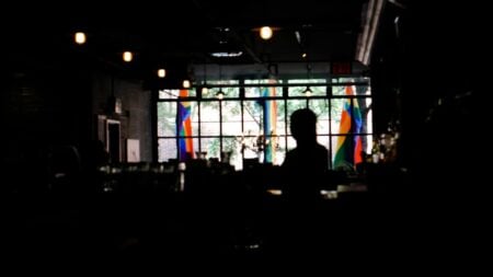Washington DC Man Accused Of Using Homophobic Slurs And Threatening Worker After Being Denied Alcohol: ‘Slurs Are Not Illegal’ bar interior with patrons visible inside while rainbow Pride flags hang in the windows.