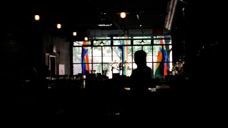 bar interior with patrons visible inside while rainbow Pride flags hang in the windows.