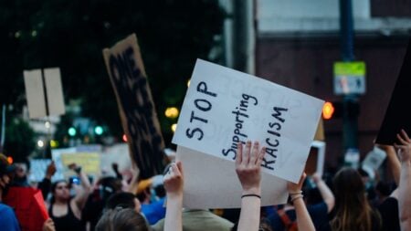 A diverse group of protesters hold signs advocating against racism in an urban setting.
