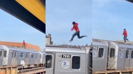 A teenager in a red hoodie standing on top of a moving New York City 7 train on an elevated outdoor track near 46th Street in Queens, filmed from a nearby platform in broad daylight.