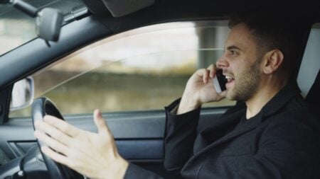 Man in car talking on cell phone while driving, displaying frustration