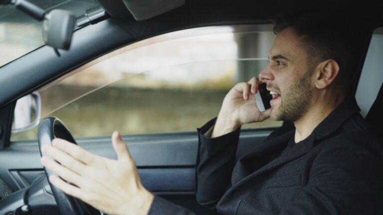 Florida Driver Left Baffled After Woman Suddenly Starts Smacking His Car: ‘What Is Even Going On?’ Man in car talking on cell phone while driving, displaying frustration