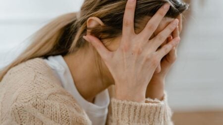 New York Man Wakes Up After Passing Out and Immediately Tries to Kiss the Woman Who Helped Him: ‘It’s Beyond Parody at This Point’ Woman sitting indoors with face covered by hands, expressing stress and frustration.