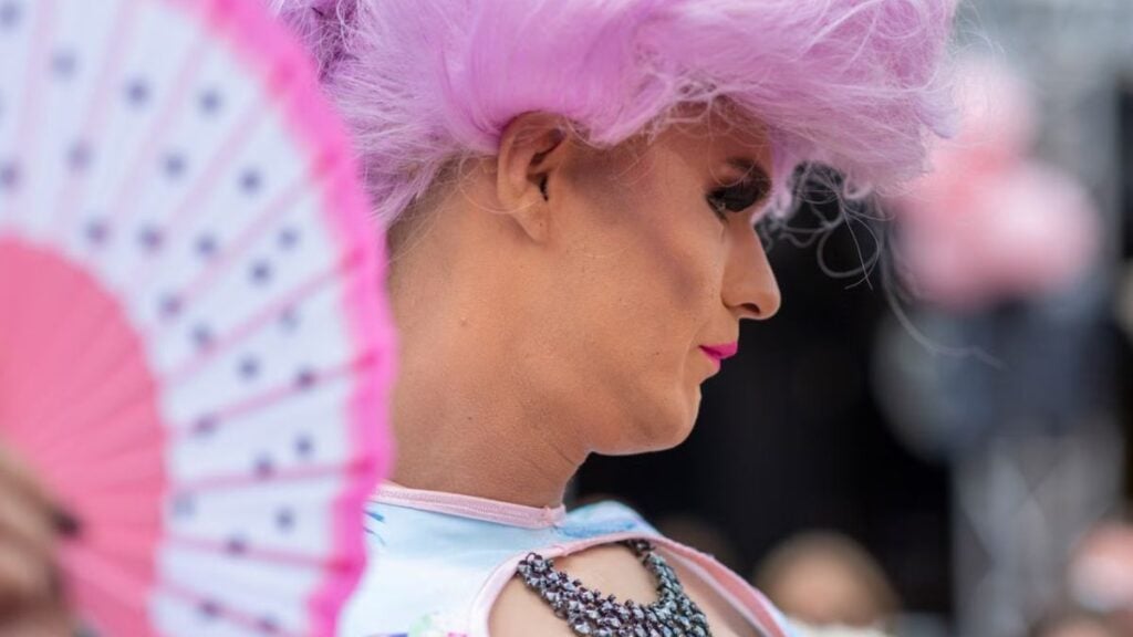 Outrage as Video Shows Drag Performers Accepting Tips From Children at Michigan Elementary School Pride Event: ‘This Is Not Okay’ A colorful drag performer with pink wig and fan at an outdoor festival, showcasing unique fashion and makeup.