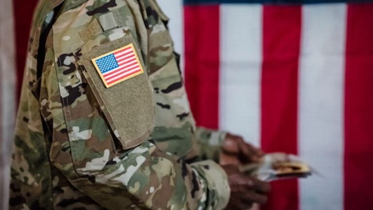 Close-up of a soldier in military uniform with American flag patch and background.