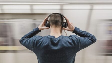 A young man wearing headphones stands in a subway station, focusing on music.