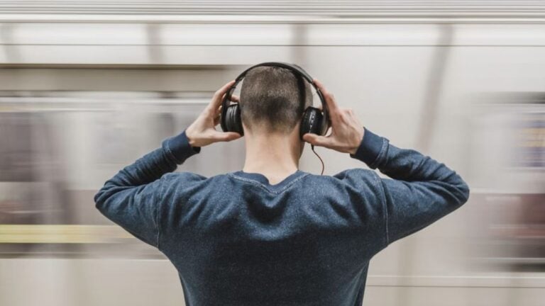 A young man wearing headphones stands in a subway station, focusing on music.