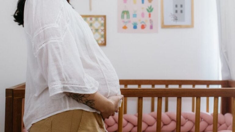California Women Arrested After Allegedly Launching Firecrackers Into Family’s Nursery And Setting It On Fire: ‘Never Forgive Creatures Like This’ Expectant mother standing beside a wooden crib in a beautifully decorated nursery room.
