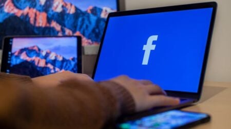 Laptop displaying Facebook at workspace with multiple devices, highlighting modern technology.