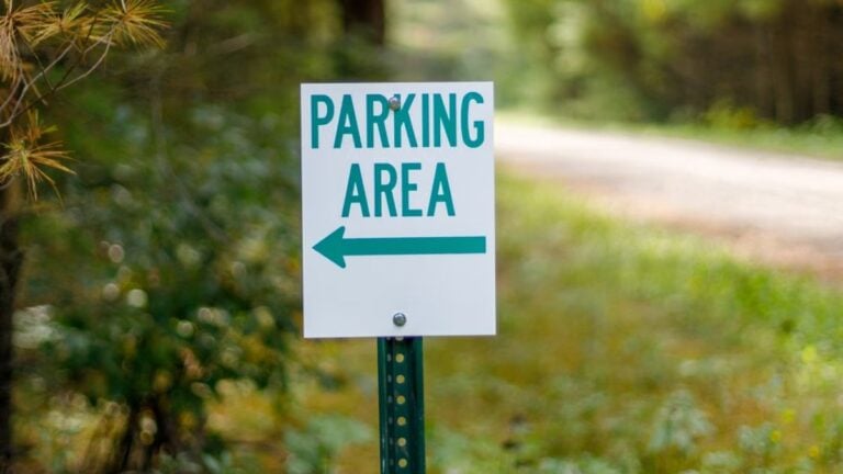 Close-up of a parking area sign with green text on a forest pathway.
