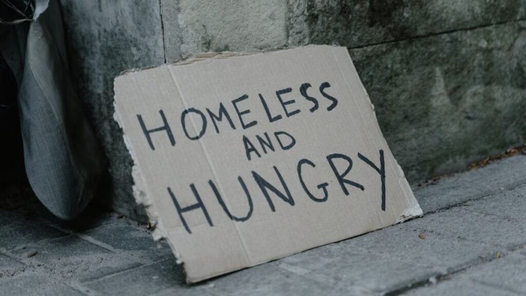 Backlash As New York Woman Says You Can Live Comfortably Without Making Anything: ‘The Homeless People On The Street Are Pretty Comfortable’ Cardboard sign with 'Homeless and Hungry' message leaning against a wall on a sidewalk.