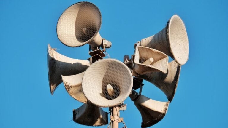Close-up of multiple aged megaphones on a pole against a clear blue sky.