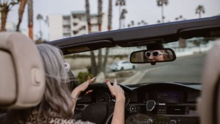 Florida Grandpa Blames Stranger for Wife’s Driving Mistake, Chases Driver Through Parking Lot: ‘Best to Just Not Engage With Boomers’ Senior woman enjoying a drive in a convertible with palm trees lining the road.