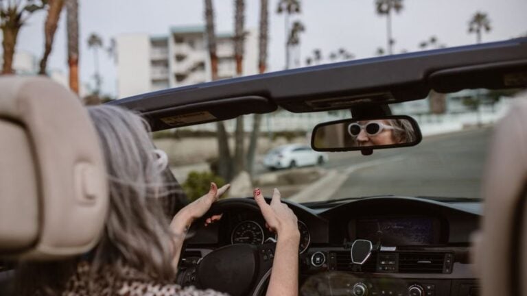 Florida Grandpa Blames Stranger for Wife’s Driving Mistake, Chases Driver Through Parking Lot: ‘Best to Just Not Engage With Boomers’ Senior woman enjoying a drive in a convertible with palm trees lining the road.