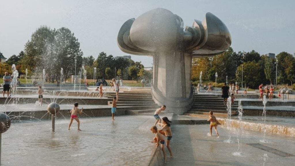 Backlash As Two Adult Men Fight at Children’s Splash Pad in North Carolina While Kids Watch: ‘This Is Trump’s America’ Happy children enjoy a sunny day playing in an urban fountain park with modern sculptures.