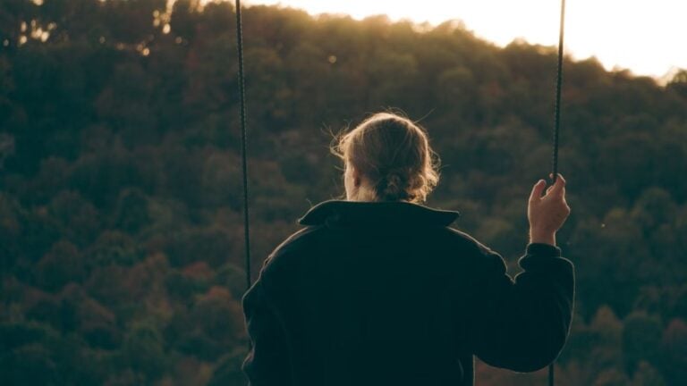 Louisiana Woman Suffers Horrific Genital Injury During Honduras Excursion, Undergoes Multiple Surgeries: ‘This Looks So Painful’ Woman in a coat swinging outdoors facing autumn forest at sunset.