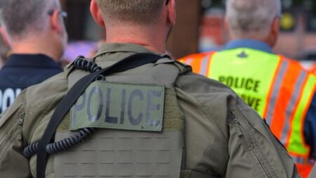 Arizona Police Tackle Black Woman Onto Metal Bike After She Approaches Arrest Scene in Tempe: ‘This Is False Imprisonment and Harassment’ Rear view of police officers in tactical gear and high-visibility vests in a public setting.