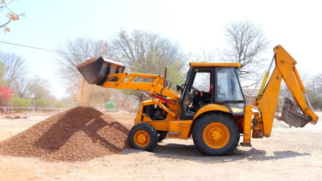 California Woman Refuses To Move Away From Excavator, Falls Into Bucket And Gets Stuck: ‘Play Stupid Games, Win Stupid Prizes’ A yellow excavator moving gravel at an outdoor construction site during the day with clear skies.