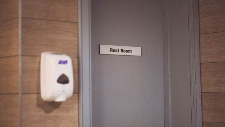 Image of a soap dispenser and a restroom door sign in a public restroom.
