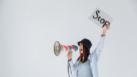 Woman passionately protesting with a megaphone and 'Stop' sign in a studio setting.