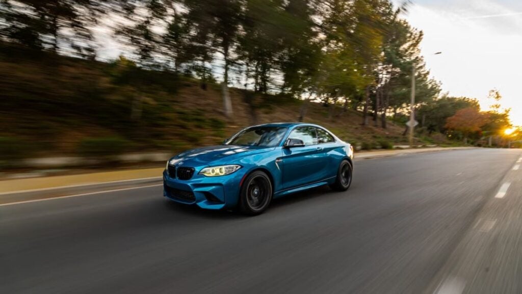 Florida Woman’s Slow Chase After Rolling Car Has the Internet Frustrated and Amused: ‘She Had a Whole Week to Save Her Car’ Dynamic motion shot of a blue sports car speeding on a scenic tree-lined road during daytime.