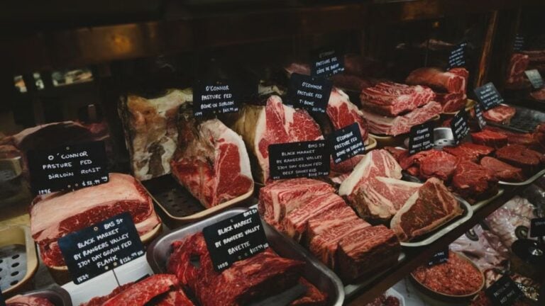 A range of raw meat cuts on display in a butcher shop, featuring labels for each type.