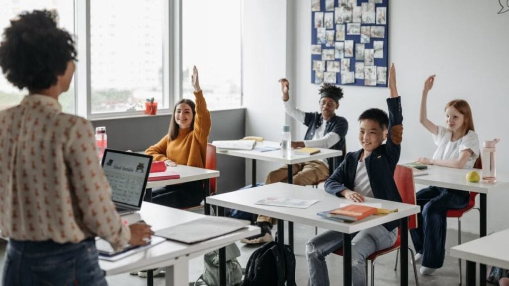 California Teacher Faces Backlash for Filming OOTD Video in Classroom on First Day of School: ‘Teachers Should Have Dress Codes’ Students in a diverse classroom eagerly raising hands during a lesson. Bright, educational atmosphere.