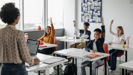 California Teacher Faces Backlash for Filming OOTD Video in Classroom on First Day of School: ‘Teachers Should Have Dress Codes’ Students in a diverse classroom eagerly raising hands during a lesson. Bright, educational atmosphere.