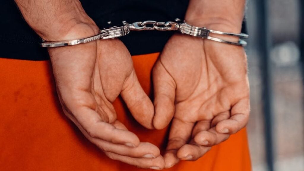 Rear view of handcuffed person in orange uniform, highlighting law enforcement and justice themes.