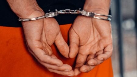 Ohio Police Handcuff 14-Year-Old Black Boy on His Front Porch Before Realizing He Wasn’t the Suspect: ‘I Didn’t Do Nothing. I’m a Kid’ Rear view of handcuffed person in orange uniform, highlighting law enforcement and justice themes.