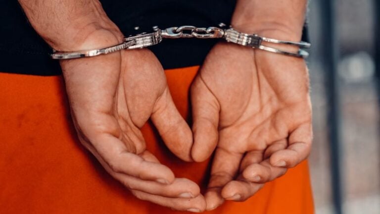 Rear view of handcuffed person in orange uniform, highlighting law enforcement and justice themes.