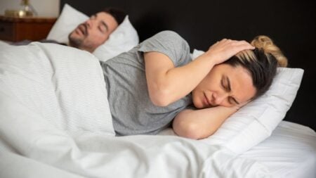 ‘How Does He Forget Something That Keeps Him From Dying?’: New Jersey Woman’s Vacation Marriage Dispute Goes Viral A woman looks frustrated in bed as her partner snores loudly, highlighting sleep disturbance issues.