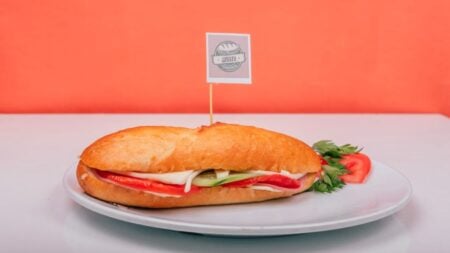 Fresh sub sandwich filled with veggies on a white plate against an orange background.