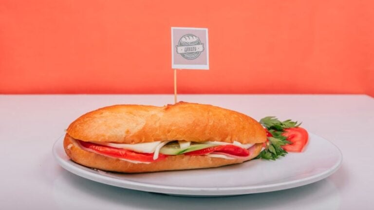 Internet Can’t Believe New Jersey Woman’s Long List of Requests for a Pork-Free Sandwich: ‘Upcharge for Every Ridiculous Demand’ Fresh sub sandwich filled with veggies on a white plate against an orange background.