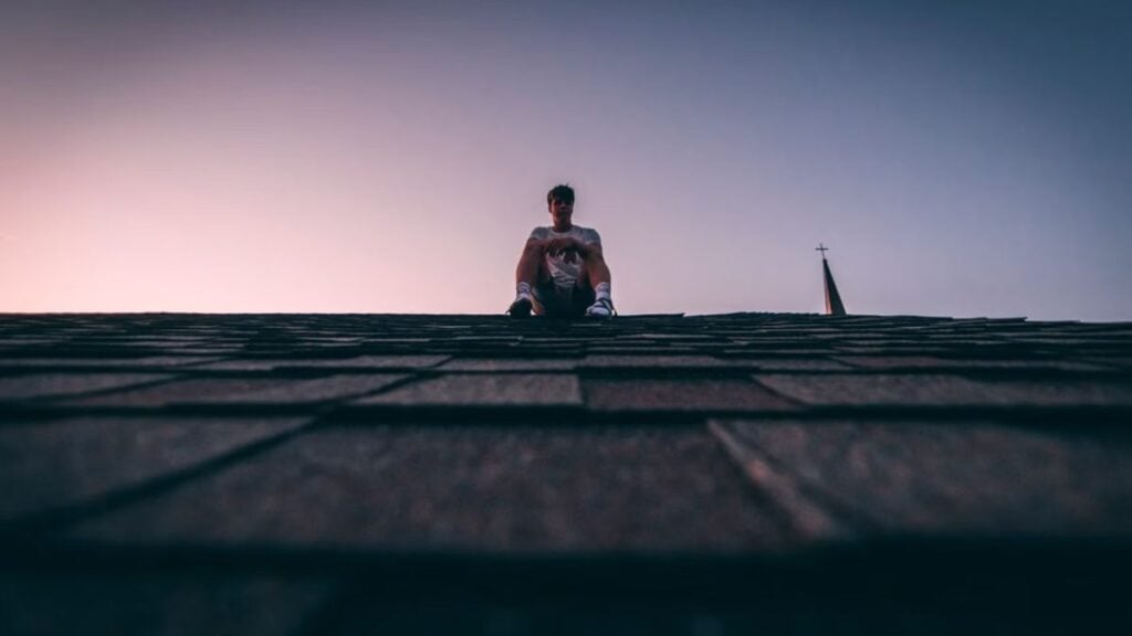 New York Man Won’t Get Off Roof Until Police Apparently Bring Him Alcoholic Beverage: ‘Bro Faked a Hostage Negotiation’ A silhouette of a man sits on a roof during twilight, backlit by a soft sky.