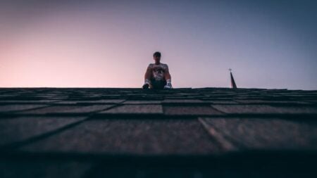 New York Man Won’t Get Off Roof Until Police Apparently Bring Him Alcoholic Beverage: ‘Bro Faked a Hostage Negotiation’ A silhouette of a man sits on a roof during twilight, backlit by a soft sky.