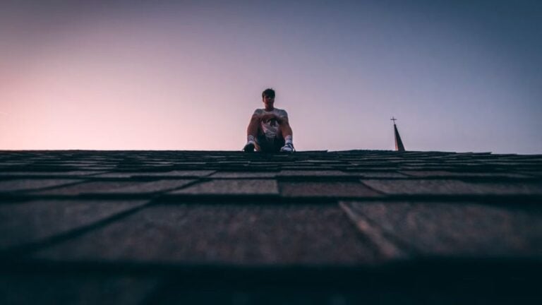 New York Man Won’t Get Off Roof Until Police Apparently Bring Him Alcoholic Beverage: ‘Bro Faked a Hostage Negotiation’ A silhouette of a man sits on a roof during twilight, backlit by a soft sky.
