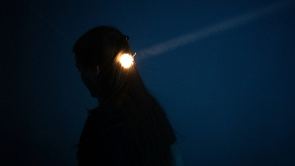 A woman standing in the dark with flashlight beams on her