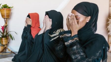 Three Muslim women in hijabs engaged in prayer indoors, showcasing unity and spirituality.